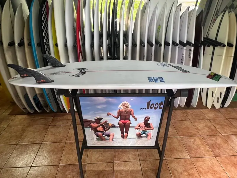 Tabla blanca sobre una mesa de exhibición Lost, con los estantes de tablas de la tienda al fondo