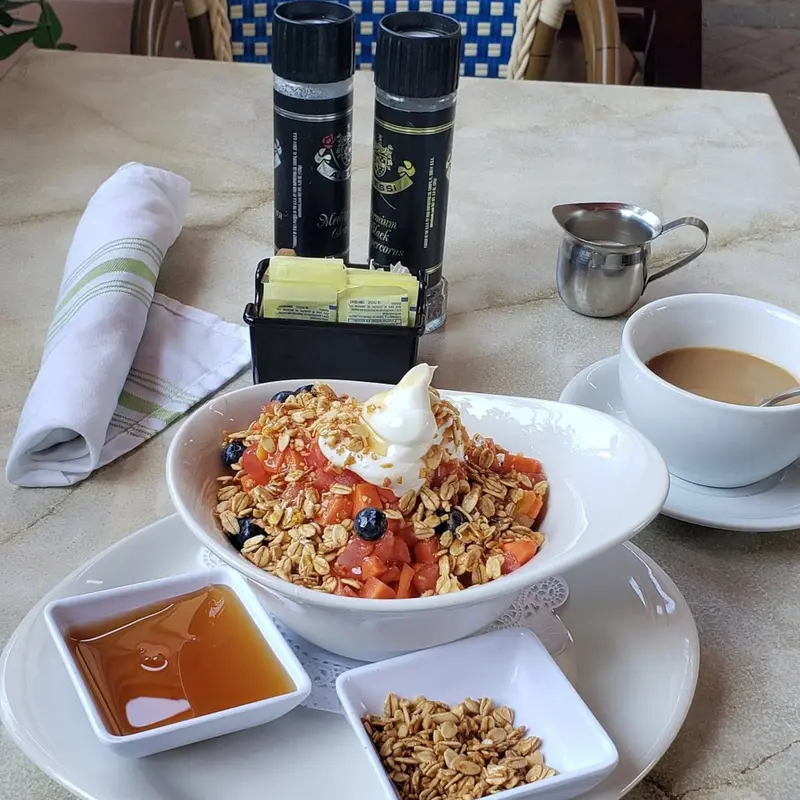 Tazón de granola con yogurt y fruta, con miel aparte y una taza de café