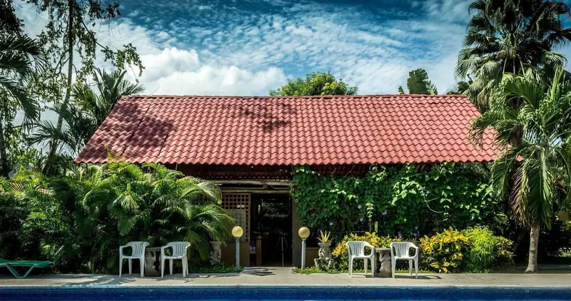 Casa de techo de teja roja entre palmeras, jardín y el borde de la piscina