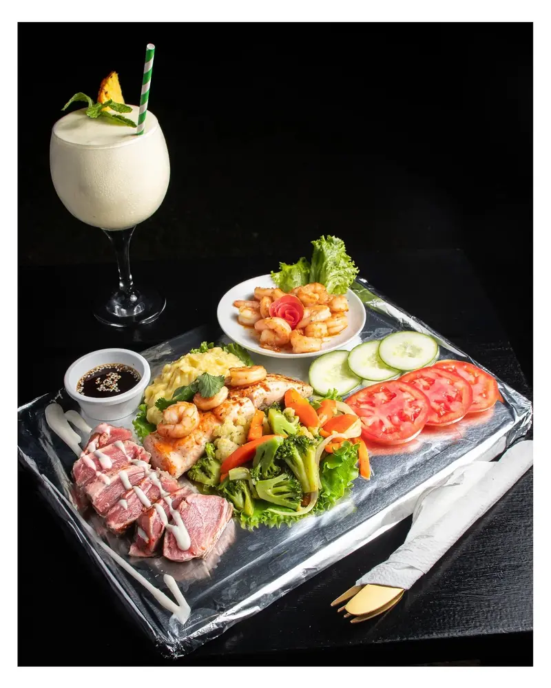 Tabla de hielo con atún sellado, camarones y vegetales, junto a un batido en copa con pajilla