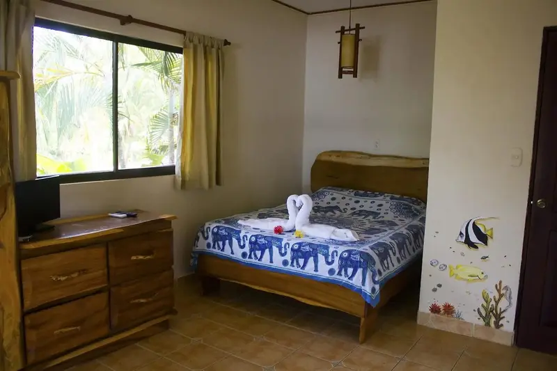 Habitación con cama de madera, cómoda con televisor, ventana con cortinas y un pez pintado en la pared