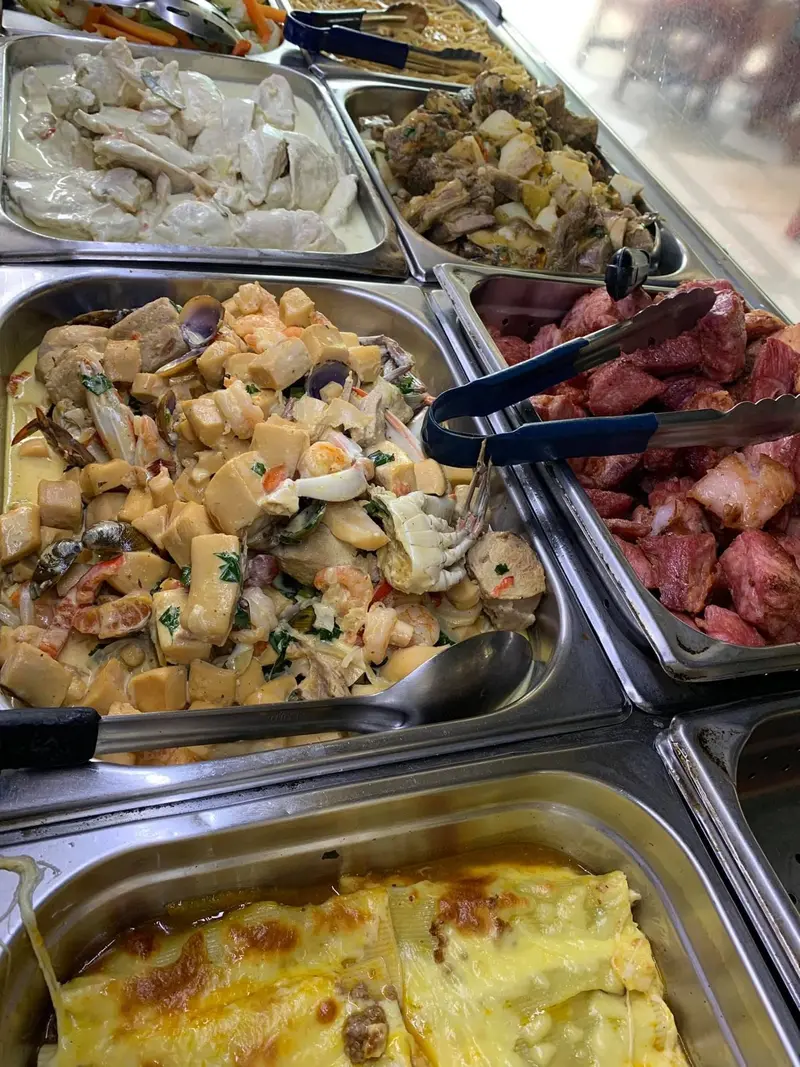 Bandejas del buffet con guisos de pollo y de mariscos con palmito, y carne en trozos