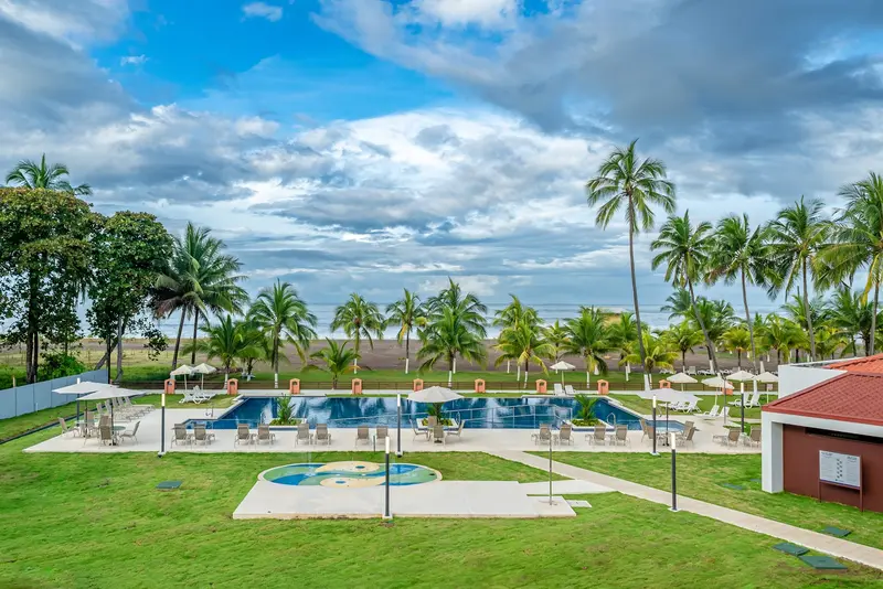 Piscina del resort frente a la playa, rodeada de jardines y palmeras