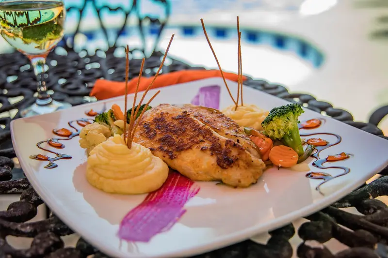 Plato blanco con un filete dorado, puré de papa y vegetales servido sobre piedras oscuras