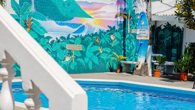 Piscina con mural de montañas, olas y flores tropicales en la pared del fondo, y una escalera blanca en primer plano