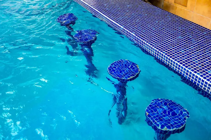 Piscina con taburetes de azulejos azules sumergidos junto a una pared de azulejos