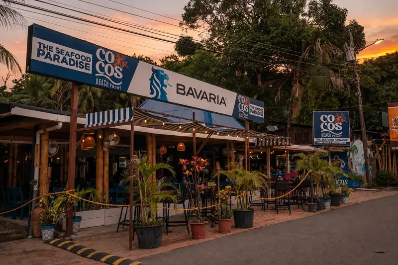 Fachada del restaurante al atardecer, con rótulos azules y una terraza cubierta junto a la calle
