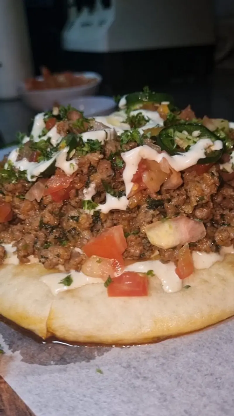 Pita abierta con carne molida, tomate y salsa blanca sobre papel