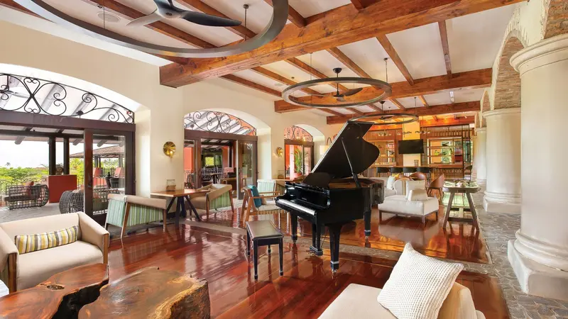 Gran salón con vigas de madera, piano de cola, pisos de madera pulida y grandes arcos abiertos