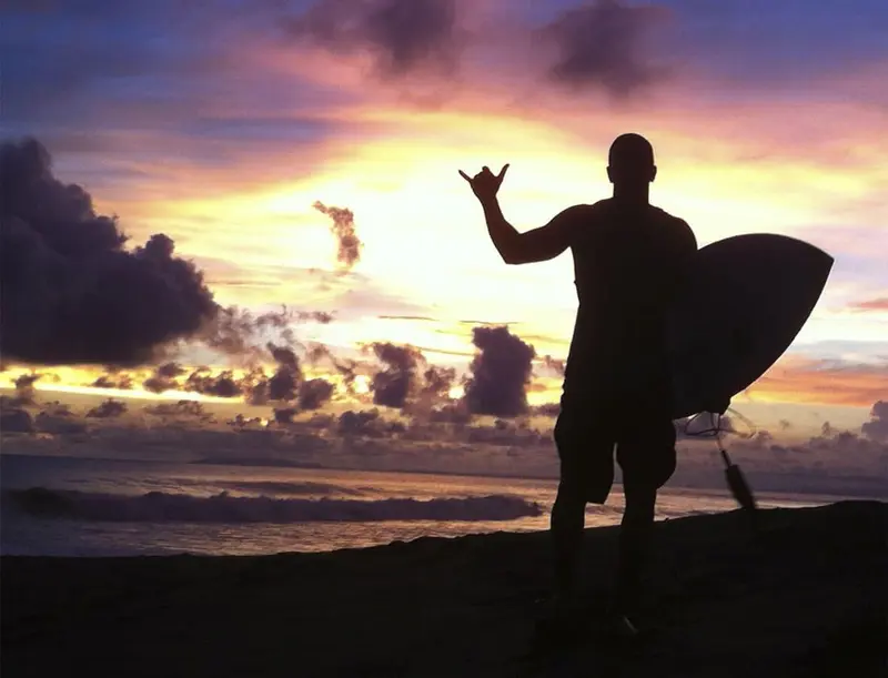 Surfer holding a board at sunset on the beach