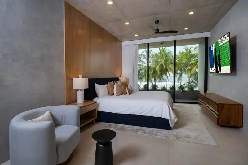 Habitación con cama king, sillón y ventanal con vista a las palmeras y la playa