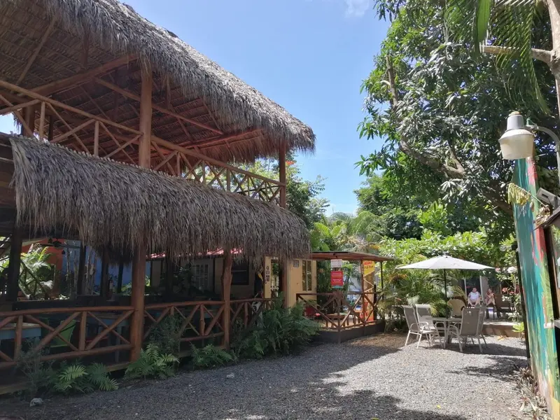 Rancho con techo de palma y barandas de madera, con mesas y sombrilla en el jardín