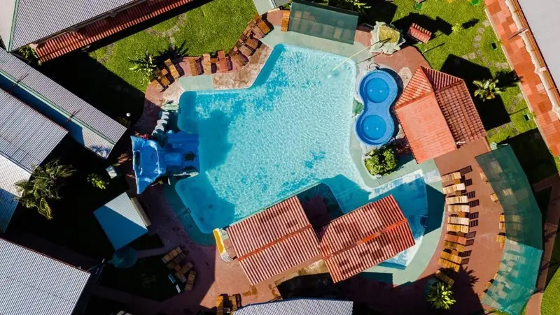 Vista aérea de la piscina con jacuzzis redondos, toboganes azules y techos de teja