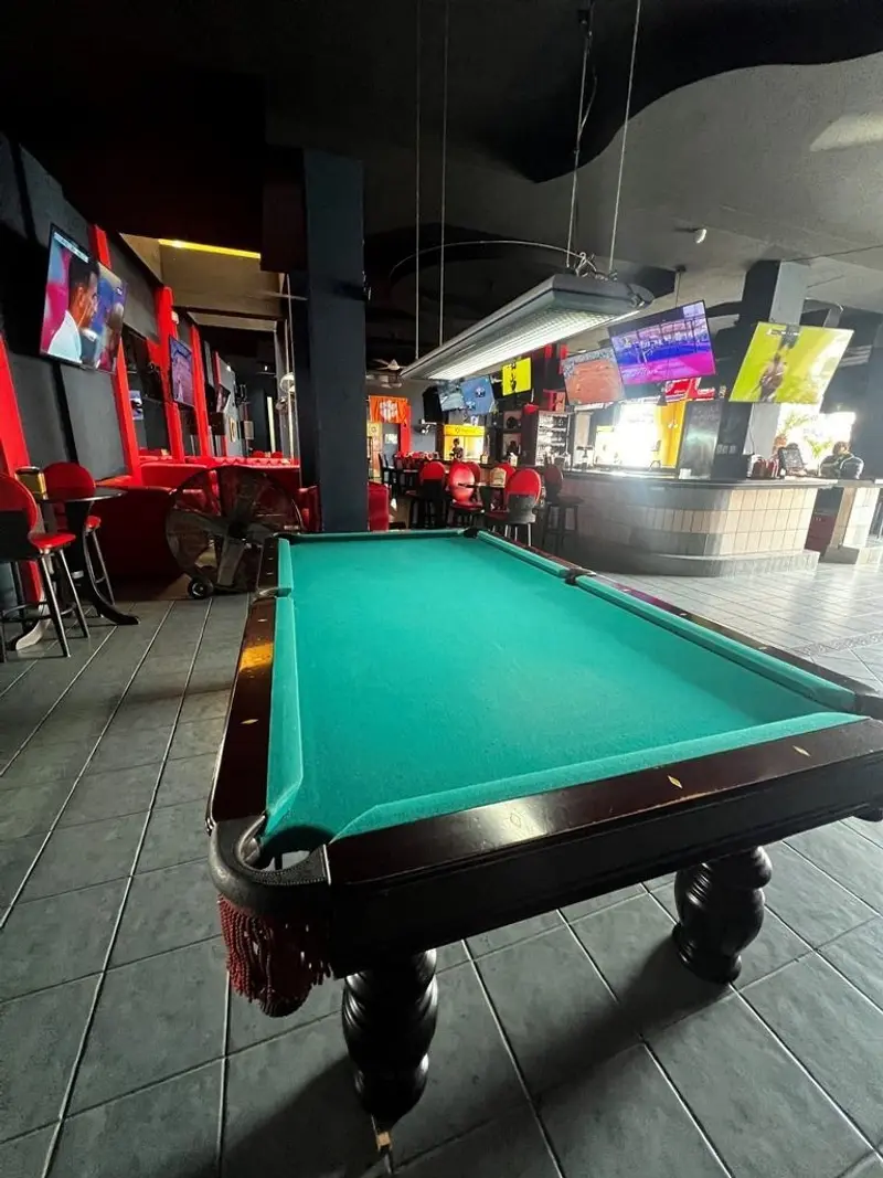 Mesa de billar verde dentro del bar, con una pantalla al fondo