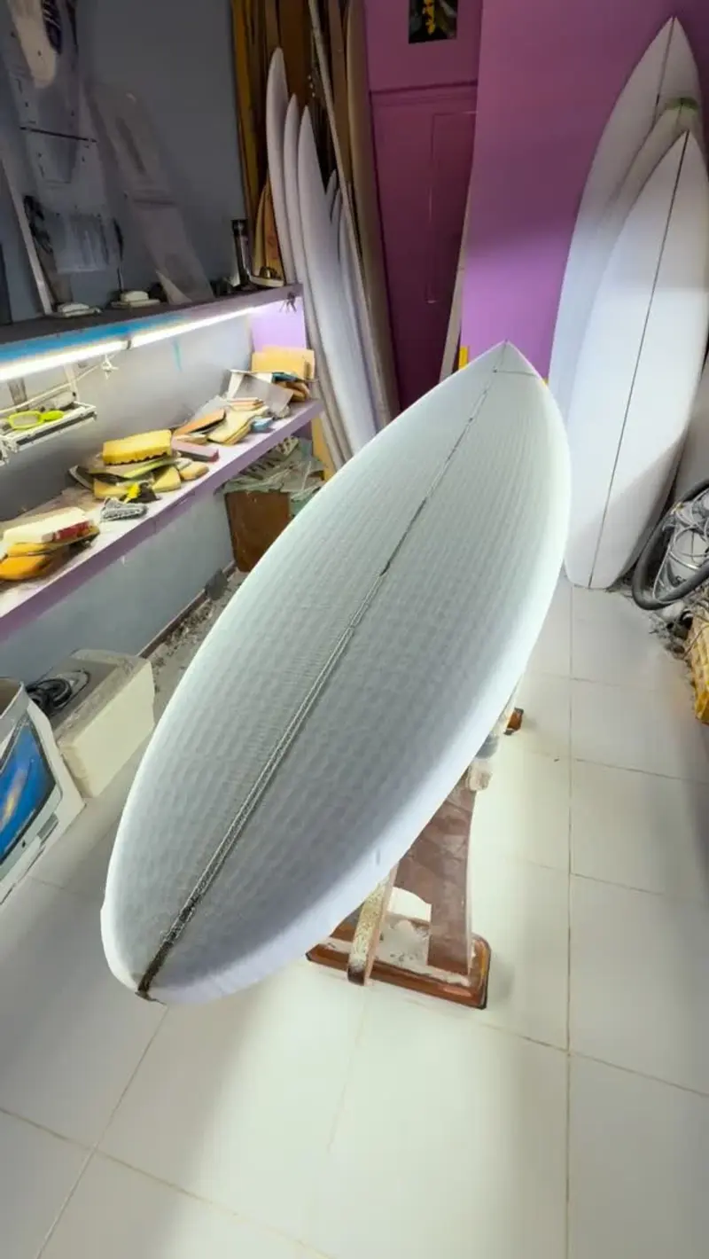 Tabla de surf blanca con rieles redondeados apoyada en la tienda, con estantes al fondo