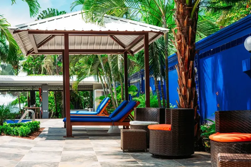 Cabana con camastros azules y sillones junto a la piscina, entre palmeras