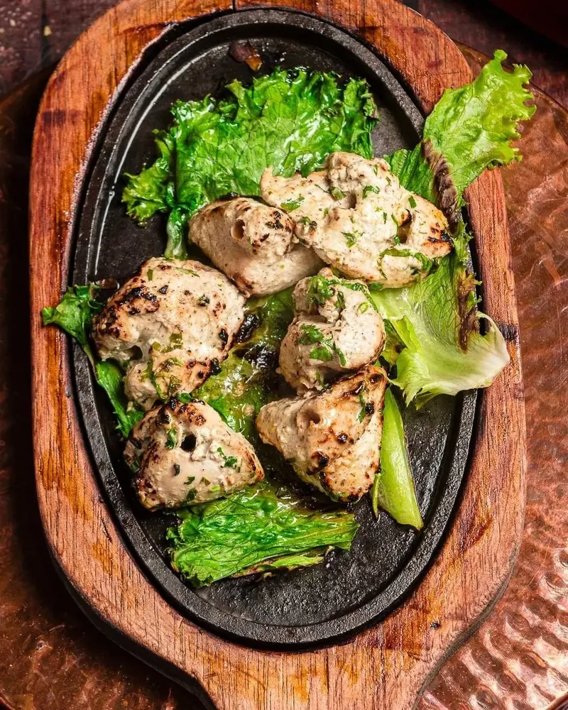 Trozos de pollo tikka sobre una plancha de hierro con lechuga, sobre una tabla de madera