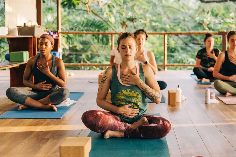 Clase de yoga en una shala abierta con vista a la selva: dos personas sentadas con las manos en el pecho sobre colchonetas