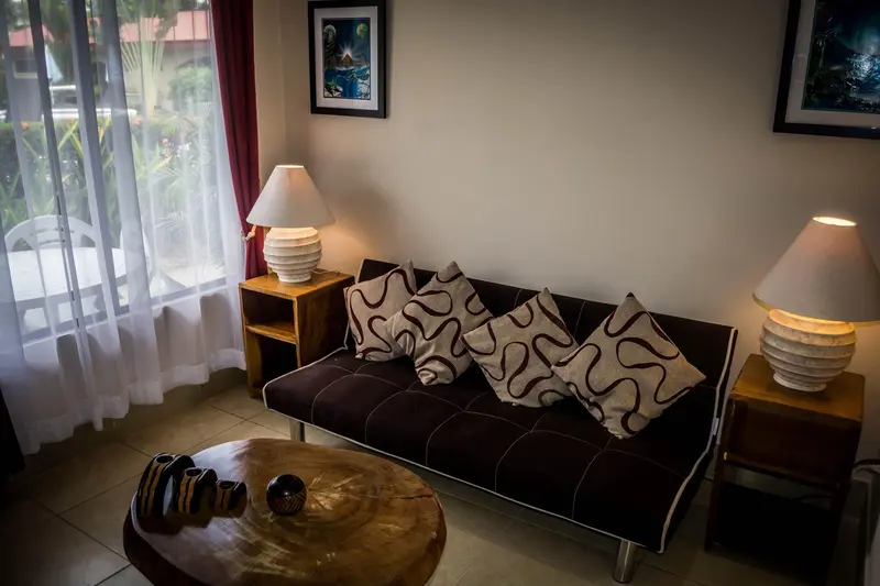 Sala con sofá de cojines estampados, mesa de madera y lámparas junto a una ventana