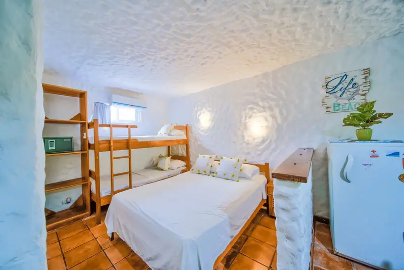 Estudio con litera de madera, cama doble y refrigerador azul, paredes blancas con relieve