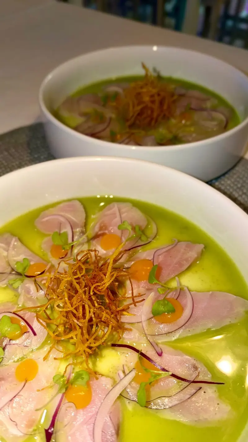 Tiradito de pescado con tiras fritas y ají sobre salsa verde en un plato hondo