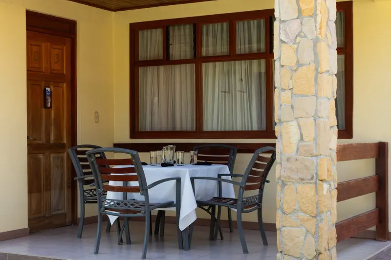 Terraza con una mesa con mantel blanco y sillas, ventanas de madera y una columna de piedra