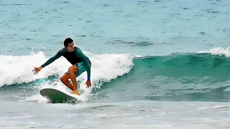 Surfista con camiseta oscura sobre una ola turquesa con espuma blanca