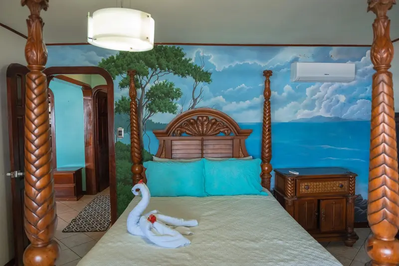 Habitación con cama de cuatro postes de madera tallada y un mural de cielo y mar en la pared