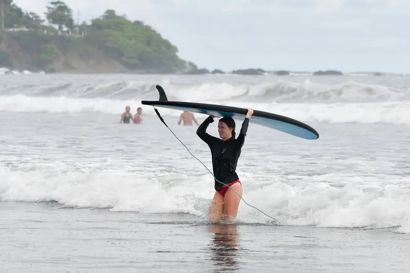 Alumna saliendo del mar con la tabla de surf sobre la cabeza
