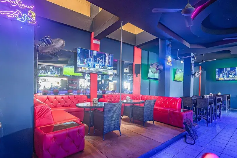 Salón del bar con sofás rojos, mesas y pantallas de televisión