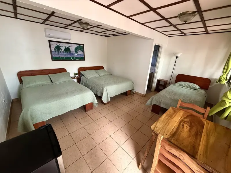 Habitación con tres camas de colcha verde, aire acondicionado y mesa de madera