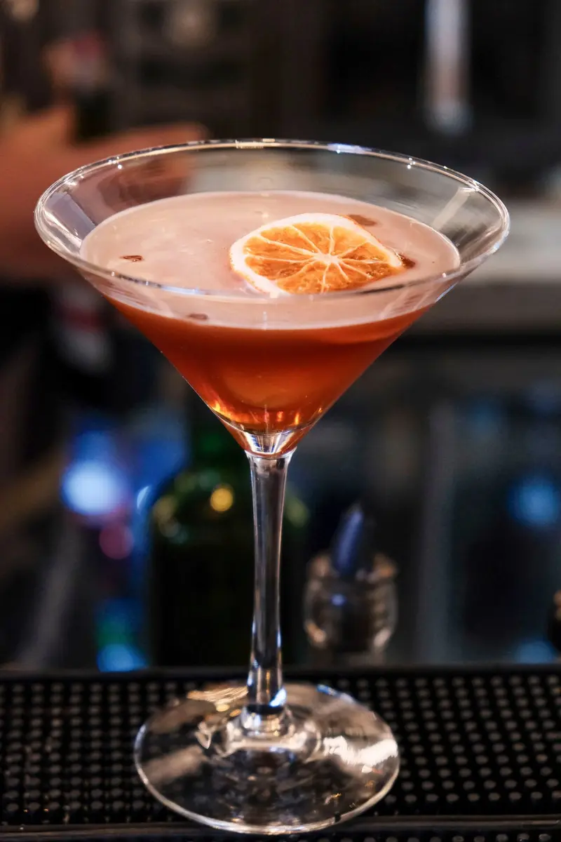 Cóctel color coral con rodaja de naranja en una copa de martini