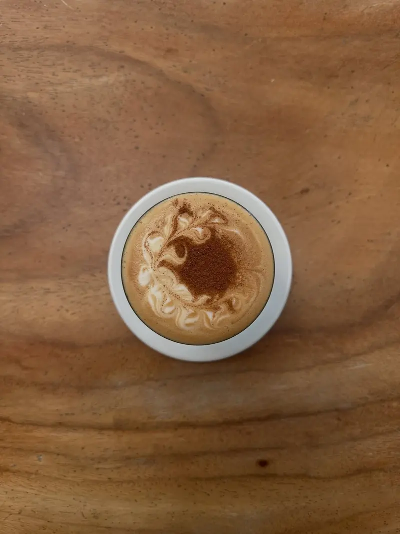 Taza de café con arte latte sobre una mesa de madera, vista desde arriba
