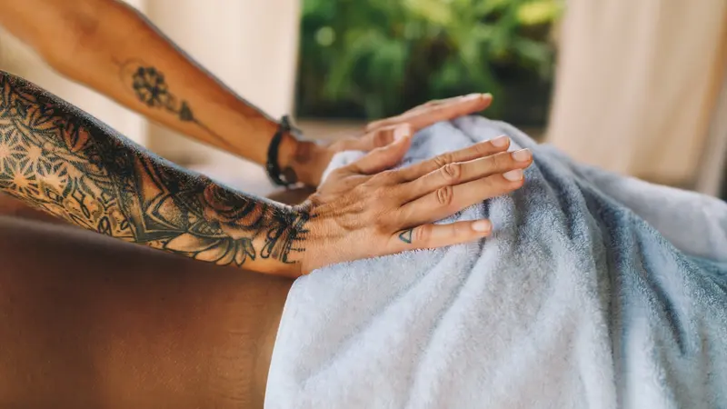 Manos tatuadas sobre una toalla durante una sesión de terapia corporal