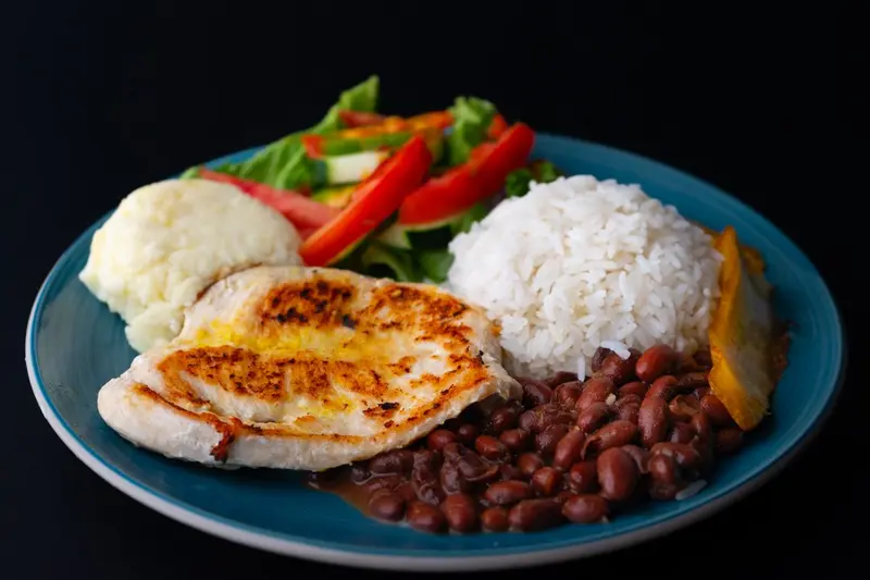 Casado con pechuga de pollo a la plancha, arroz, frijoles, ensalada y puré en un plato azul