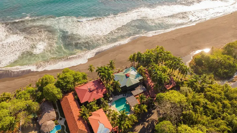 Vista aérea de la playa de arena oscura y los techos rojos del hotel entre la vegetación
