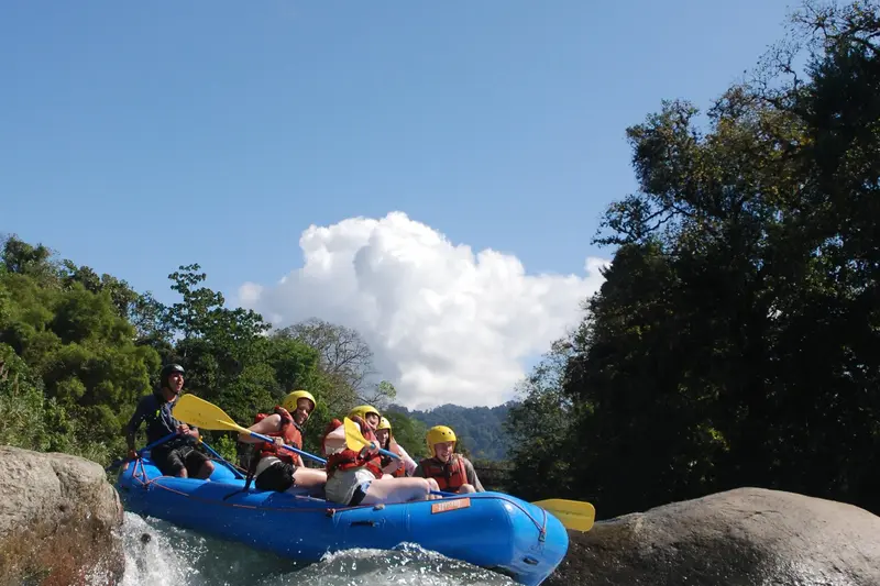 Balsa azul saltando una caída del río con rafters de casco amarillo bajo un cielo azul