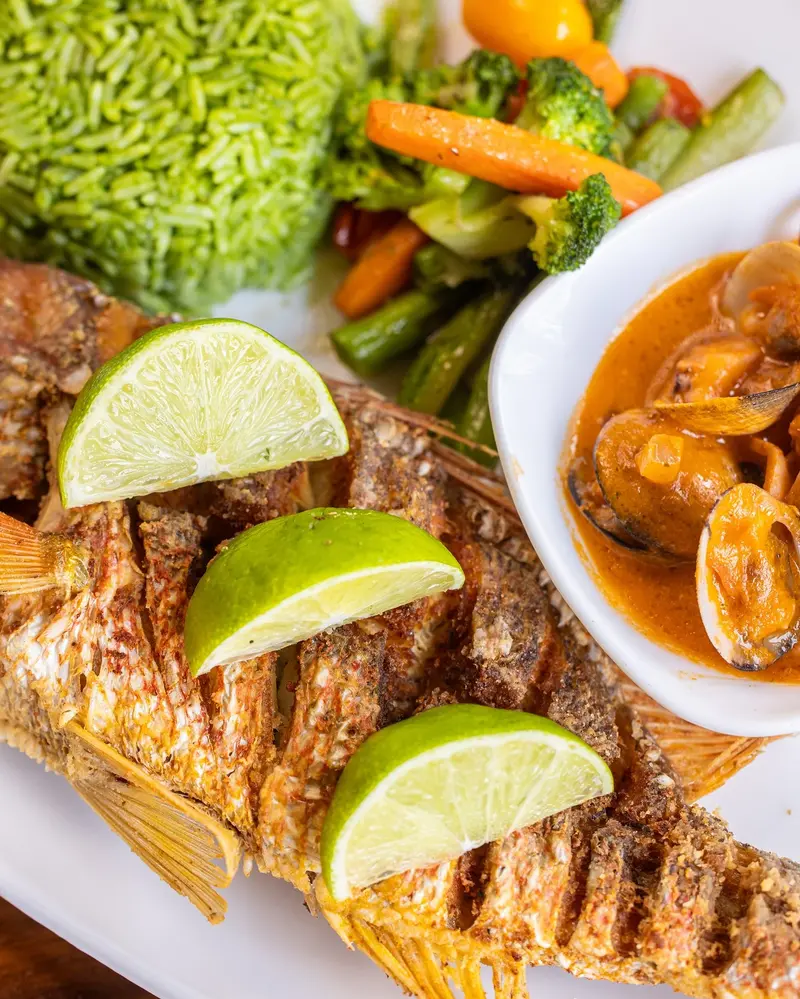 Pargo entero a la parrilla con limones, arroz verde, vegetales y un bol de mariscos en salsa