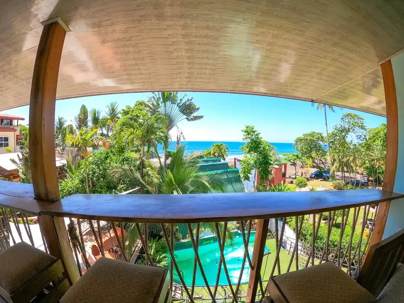 Balcón con barra de madera y vista al mar, la piscina y las palmeras