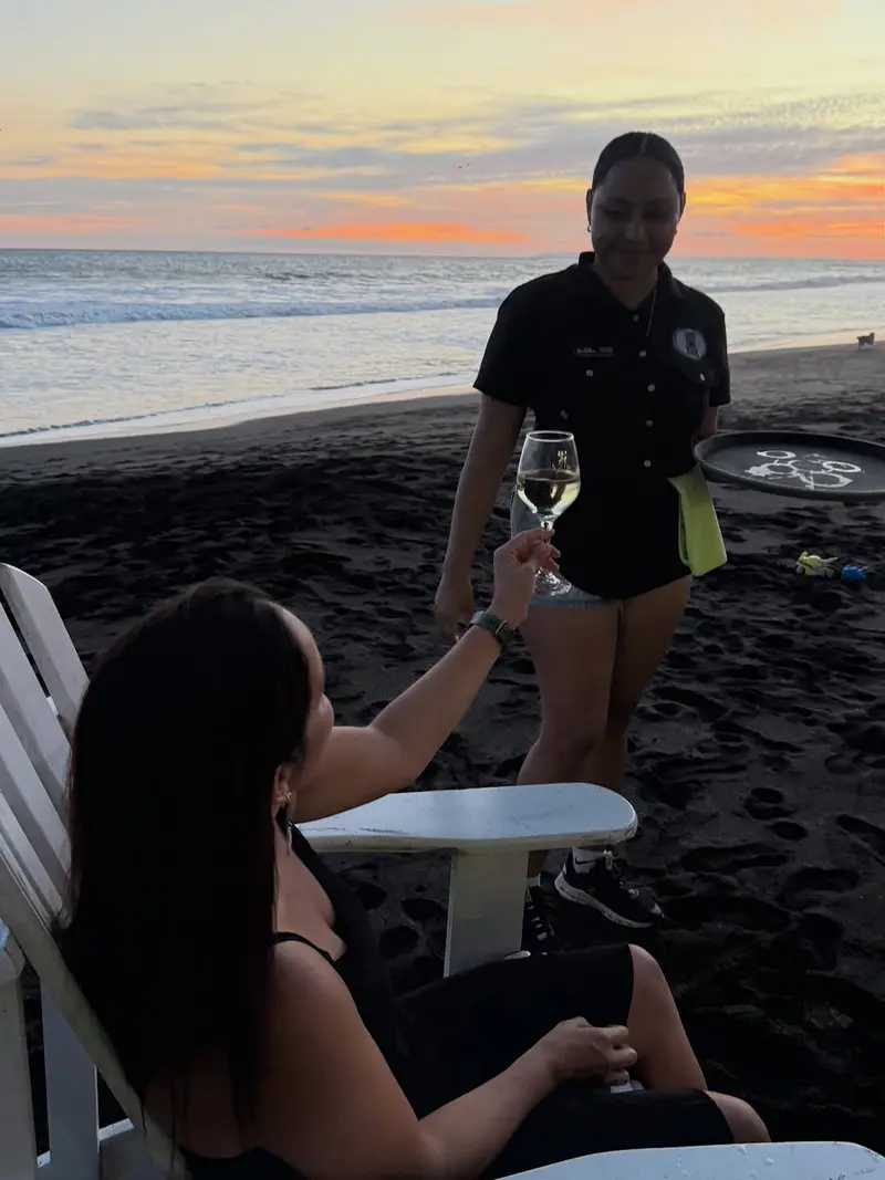 A server delivering a glass of wine right on the beach at sunset, Vida Hermosa