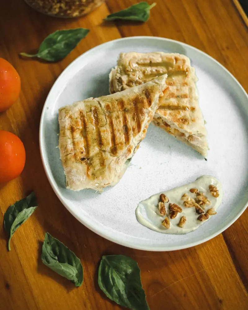 Sándwich tostado cortado en dos sobre un plato, con hojas de albahaca y mandarinas alrededor