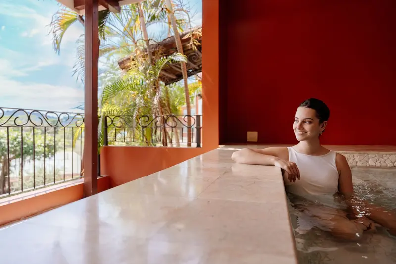Mujer en el jacuzzi del spa junto a un balcón con palmeras