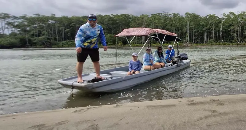 Lancha con toldo avanzando por un río con manglar, con pasajeros a bordo