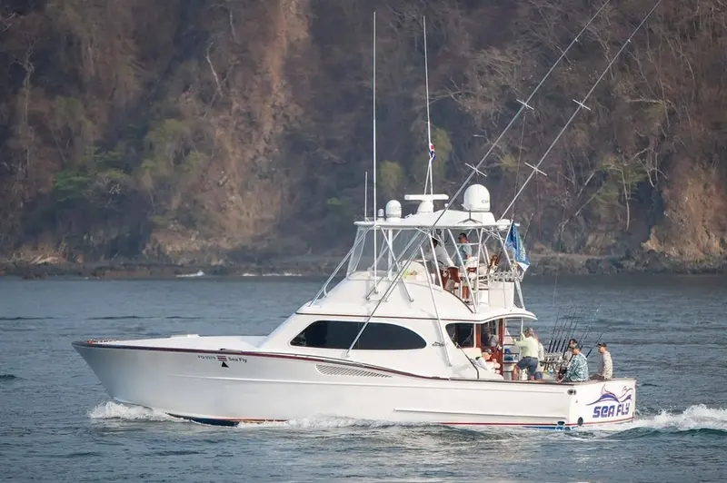Barco de pesca blanco con torre navegando sobre el mar, con la costa al fondo