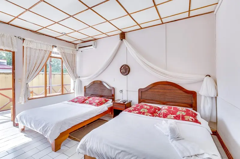 Habitación con dos camas de cubrecamas rojos, un dosel blanco y ventanas con cortinas