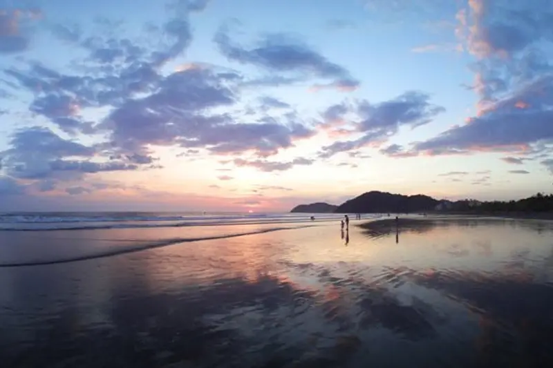 Playa al atardecer con nubes rosadas reflejadas en la arena mojada