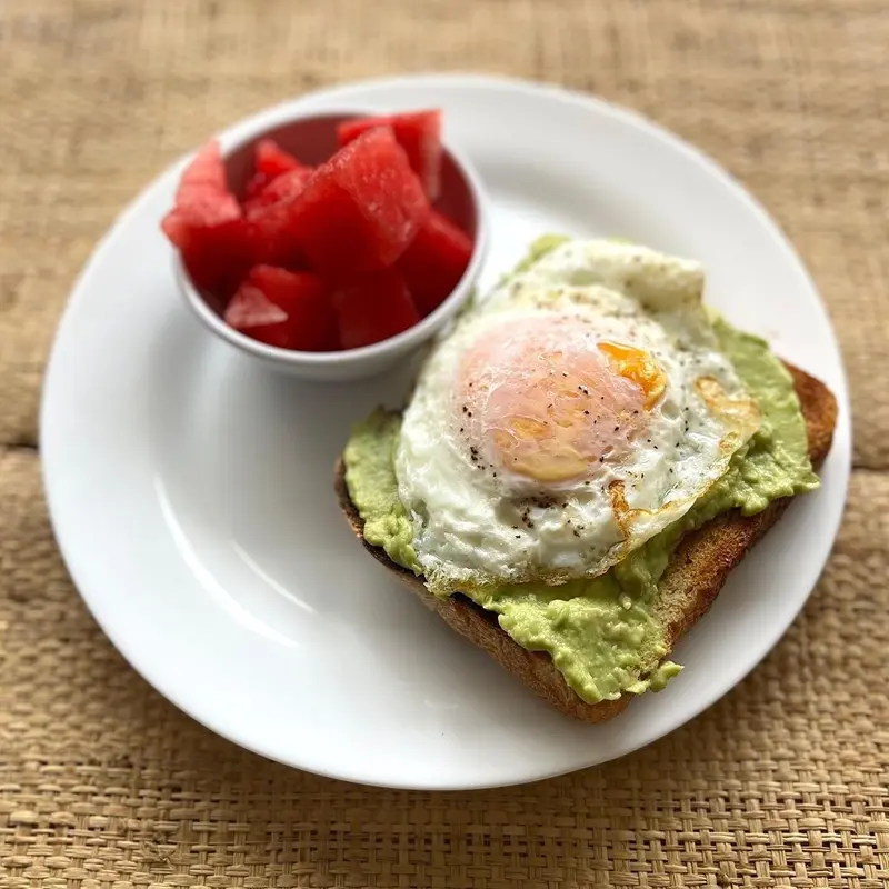 Tostada de aguacate con huevo frito y un bol de sandía