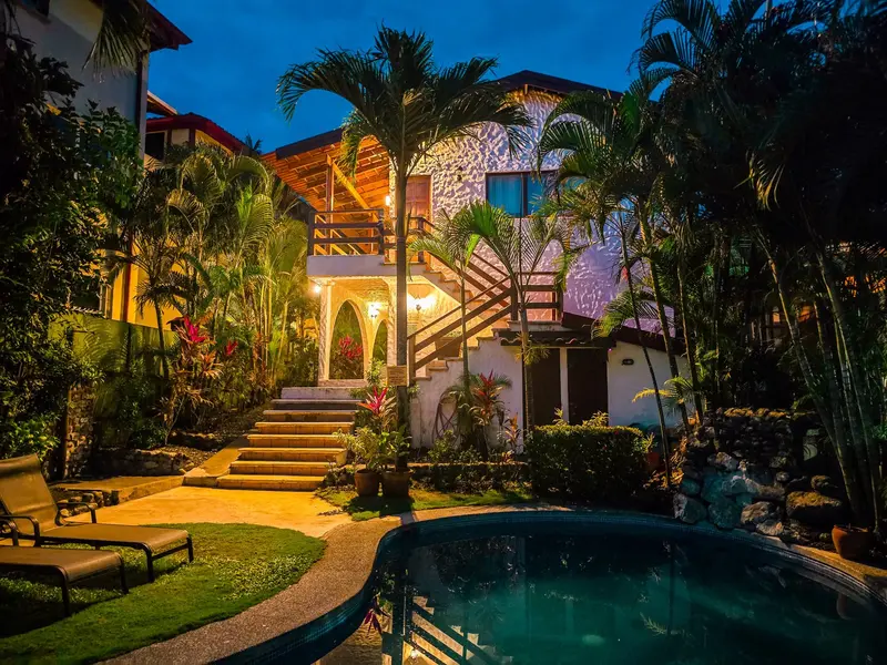 Edificio con escalinata y palmeras al atardecer, junto a la piscina iluminada