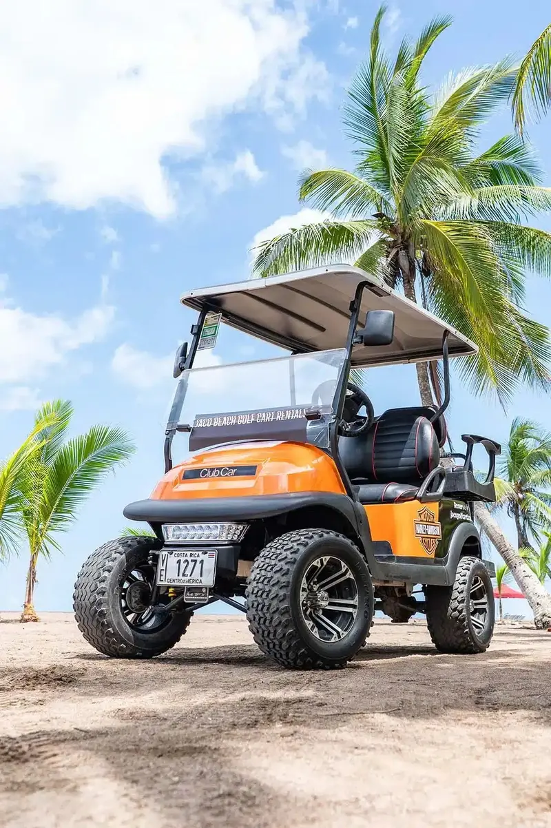 Carrito de golf naranja con parabrisas sobre la arena y palmeras al fondo