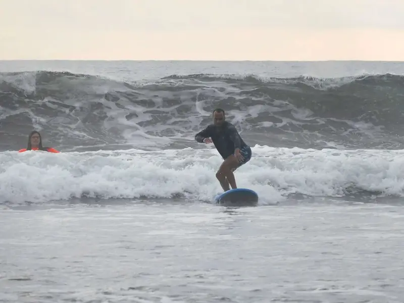 Surfista de pie sobre una tabla en una ola pequeña de agua gris